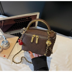 Detail of a brown woven box bag with a gold metal handle and cherry pendant