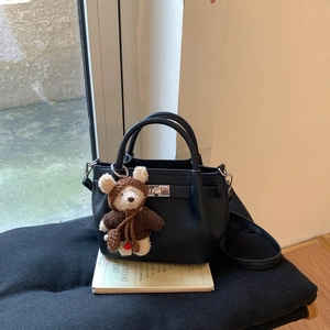 Detail of black lychee grain leather handbag featuring metal clasp and plush bear charm