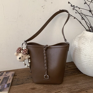 Detail of dark brown leather bucket bag featuring woven trim and cute plush bear charm