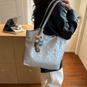 Detail of silver metallic tote bag with plush bear charm in a lifestyle office setting
