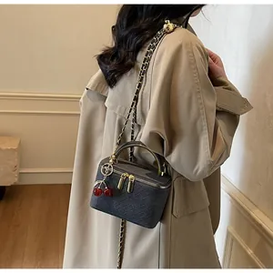 Detail shot of grey woven box bag featuring gold handle and red cherry charm
