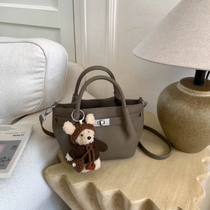 Detail of tan pebble leather mini tote with metal clasp and cute bear charm accessory
