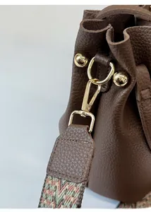 Close-up of brown litchi leather bucket bag with gold hardware and woven geometric strap