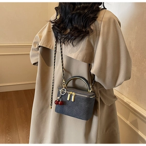 Detail of dark grey woven crossbody bag with gold handle and cherry charm on a model