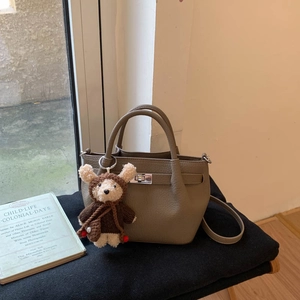 Detail of khaki pebbled leather bucket bag with metal clasp and plush bear charm