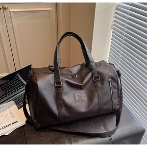Détail du sac de voyage en cuir marron foncé texturé avec poignées et logo chic
