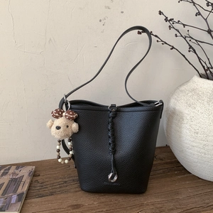Close-up of black lychee grain bucket bag with woven detail and plush bear charm