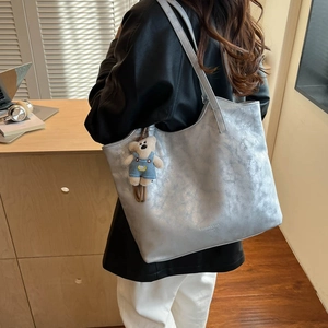 Detail of silver leather tote bag with fashion lettering and cute bear charm accessory