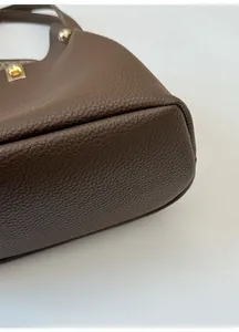 Detailed close-up of brown litchi grain leather bucket bag with gold twist lock hardware