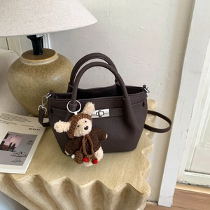 Detail of dark brown lychee leather tote bag featuring silver metal twist lock and bear charm