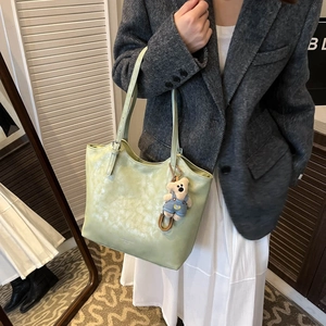 Detail of light green tote bag featuring synthetic leather texture and a cute bear charm
