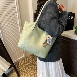 Close-up of light green textured tote bag featuring a cute bear charm and logo detail