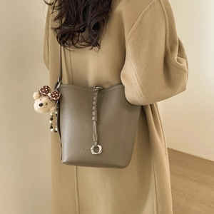 Close-up of brown pebbled leather bucket bag with woven trim and cute bear charm