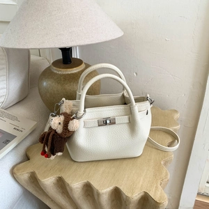 Detail of white lychee leather bucket bag with metal twist lock and cute monkey charm