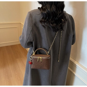 Detail of a brown quilted box bag featuring a metal handle and cherry charm accessory