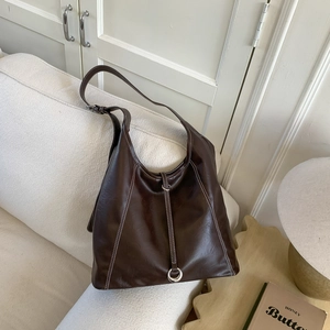 Detailed view of dark brown leather tote bag with white contrast stitching on a sofa