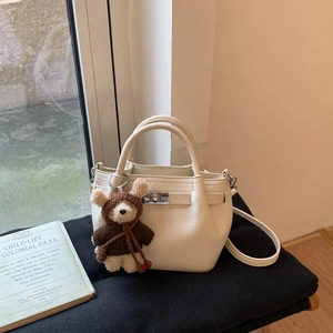 Detail of cream pebble leather bucket bag with metal lock and cute bear charm