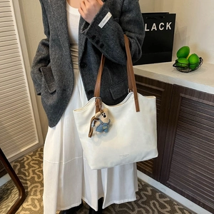 Detail of white leather tote bag with brown straps and cute bear charm in stylish setting