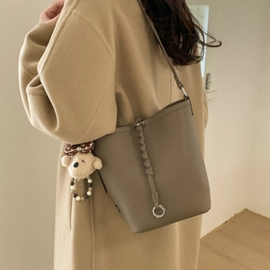 Detail of coffee bucket bag with litchi texture leather and teddy bear charm