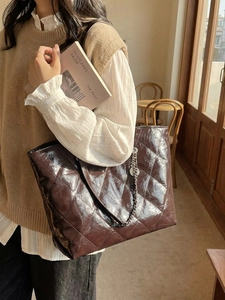 Brown quilted tote bag with glossy finish and chain detail shown in a cozy indoor setting