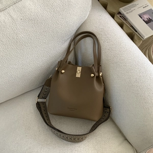 Detail of dark brown lychee leather bucket bag with gold twist lock and woven shoulder strap