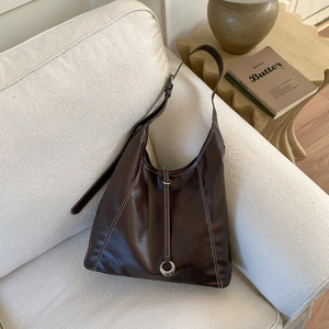 Detail of dark brown hobo tote bag featuring contrast stitching on a soft sofa