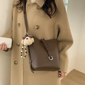 Detail of dark brown leather bucket bag with litchi texture and cute bear charm