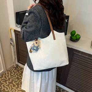 Detail of white textured leather tote bag with brown strap and cute teddy bear charm