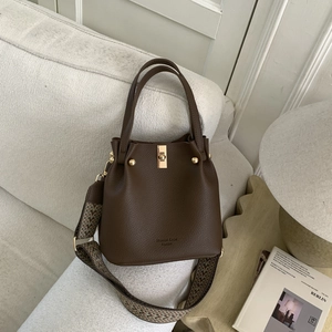 Detail of brown litchi leather bucket bag with wide geometric strap on sofa