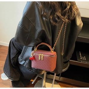 Close-up of wine red woven lattice crossbody bag with cherry charm and chain strap