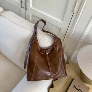 Detail of a brown tote bag with white contrast stitching and silver metal ring accents