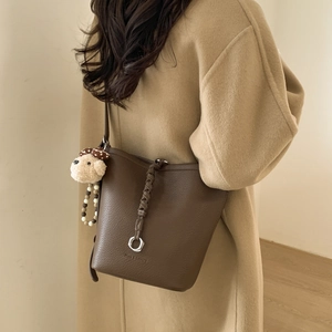 Detail view of dark brown bucket bag with lychee texture and cute plush puppy charm