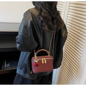 Detail of burgundy box bag with woven texture, gold handle and cherry charm detail