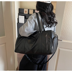 Vue latérale d'un grand sac de sport en similicuir noir porté par un mannequin en intérieur
