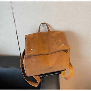 Detail of a brown suede backpack featuring a minimalist flap and silver metal rivets