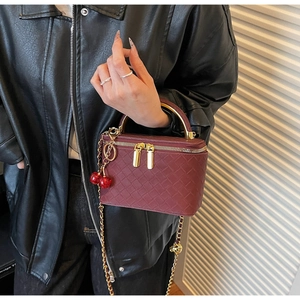 Detail of burgundy woven box bag with gold metal handle and cherry charm decoration