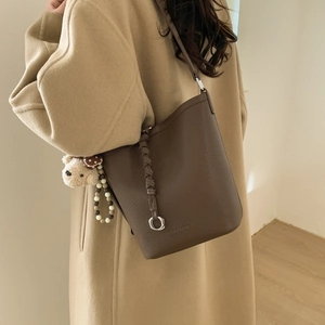 Detail of dark brown pebble leather bucket bag with teddy bear charm and braided strap
