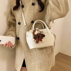 Detail of off-white leather bucket bag with metal twist lock and cute bear charm