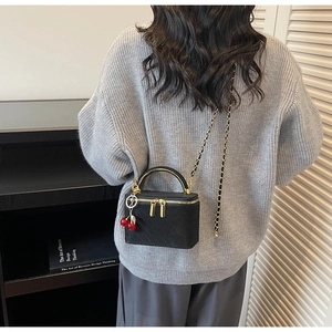 Detail of black lattice box bag with gold metal handle and cherry charm worn by model