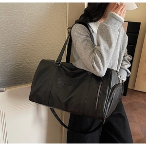 Détail du sac de sport en cuir noir montrant le logo embossé et la bandoulière réglable