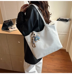 Detail of white leather tote bag featuring a plush bear charm and fashion logo stamp