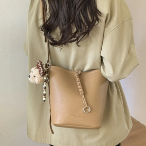 Close-up of bucket bag showing litchi grain leather texture and plush bear pendant