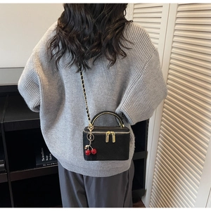 Detail of black quilted vanity bag with golden handle and cherry charm on model