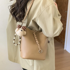 Close-up of khaki pebbled leather bucket bag featuring a cute dog charm and pearl chain