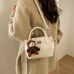 Close-up of off-white lychee leather bucket bag with silver turn-lock and bear charm