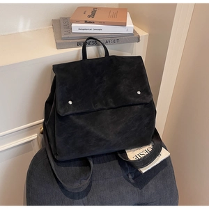 Detail of black matte suede backpack with silver cylindrical buckles on a fabric stool
