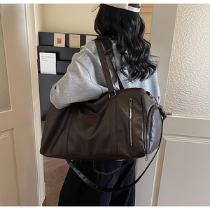 Détail du sac de sport en cuir marron foncé montrant la texture et la fermeture éclair