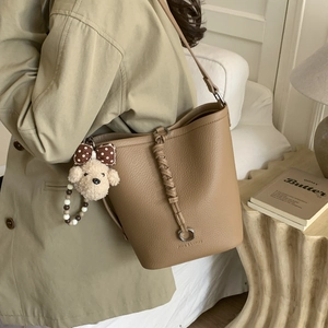 Close-up of brown pebbled leather bucket bag with dog plush charm and woven strap detail