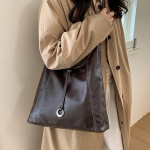 Detail of dark brown tote bag with white contrast stitching and silver metal ring