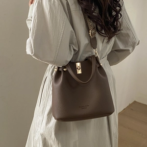 Detail of lychee pattern leather bucket bag with gold turn-lock and woven strap